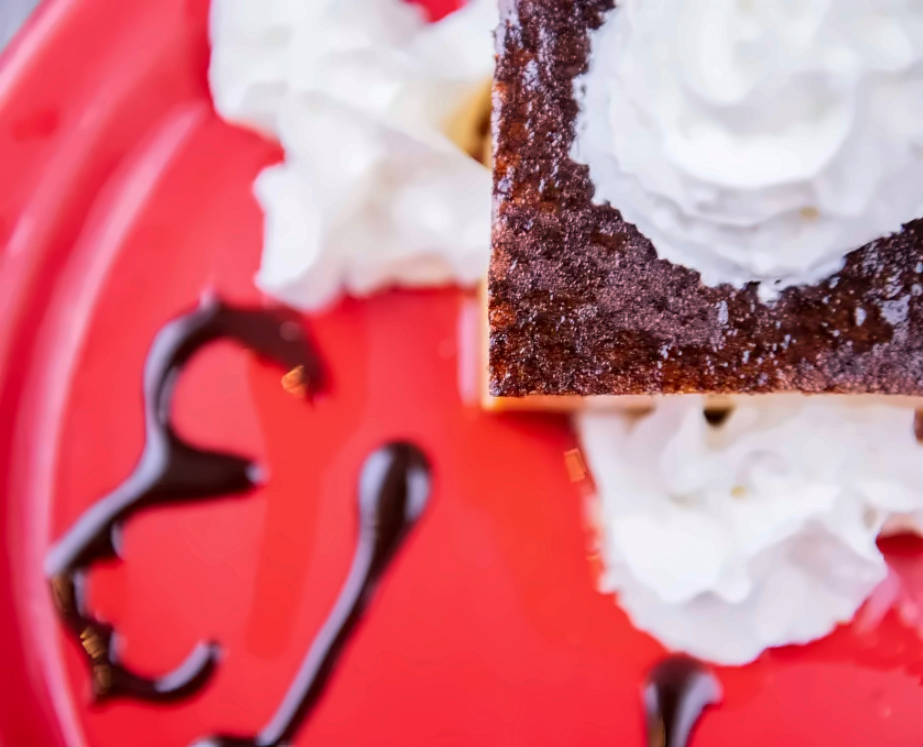 Flan with whipped cream and chocolate drizzle on a red plate