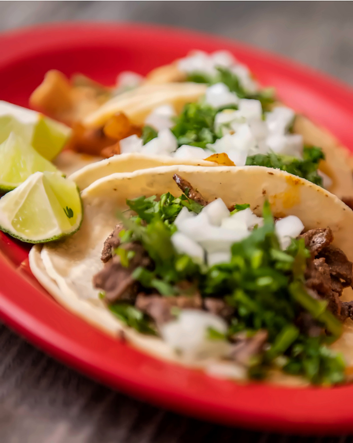 Steak and al pastor street tacos with onions, cilantro and lime on a red plate