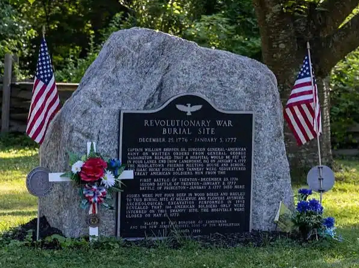 Granite memorial stone with a bronze plaque, flanked by American flags, at the Revolutionary War burial site
